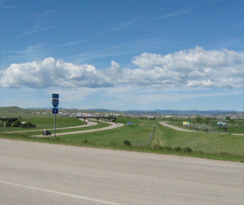 Interstate 90 West sign and interchange ramps with Rapid City in the distance